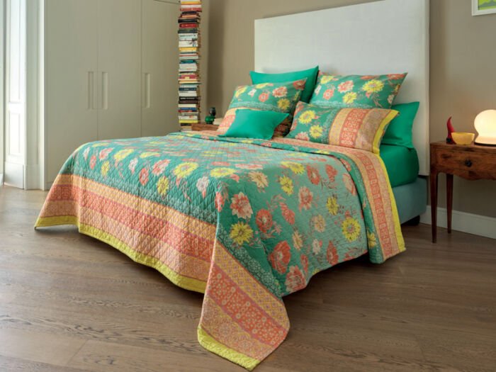 Bett mit weißem, hohem Kopfteil und grüner gesteppter Tagesdecke mit Blumenmotiv