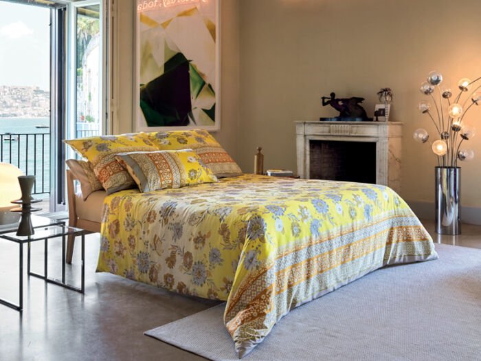 Schöner Raum mit Bett, auf dem eine gelbe Bettwäsche mit floralem Muster liegt