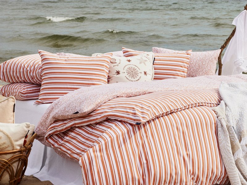 Orange-weiß gestreifte Bettwäsche mit Dekokissen auf einem Bett am Strand